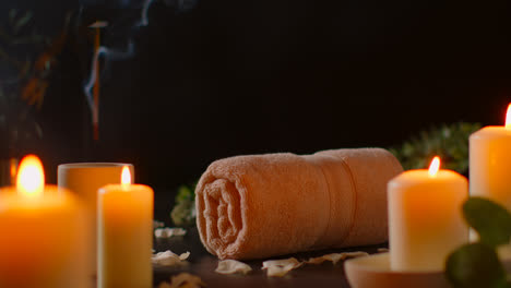 Still-Life-Of-Lit-Candles-With-Scattered-Petals-Incense-Stick-And-Soft-Towels-Against-Dark-Background-As-Part-Of-Relaxing-Spa-Day-Decor